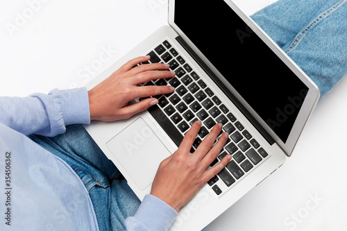 A young girl in jeans sits with a laptop on her lap. Isolated on a black screen. Blogging and communication. White background. Space for text.