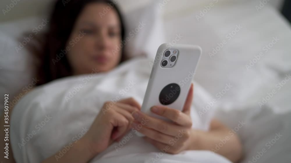 Woman lying in bed using mobile phone, shallow depth of field Woman lying in bed using mobile phone, shallow depth of field