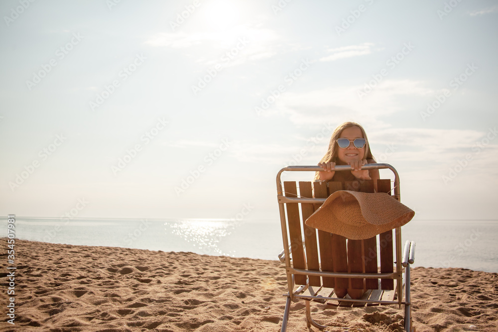 Preteen girl in straw hat relax on the beah in deck chair