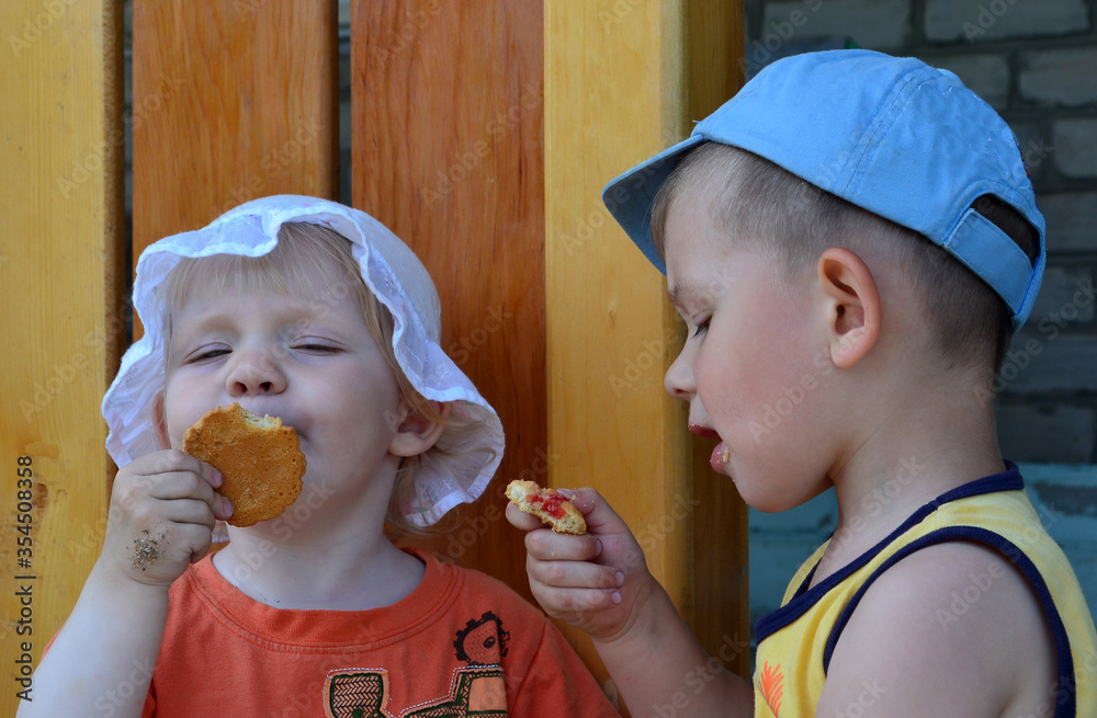 Happy caucasian children sitting in the yard and eating cookies together in summer lifestyle Happy caucasian children sitting in the yard and eating cookies together in summer lifestyle