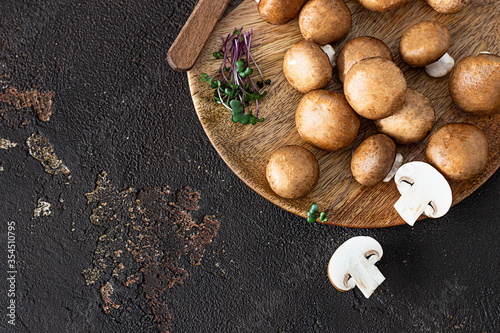 Fresh champignon on wooden plate, dark brown texture background. Brown mushrooms.