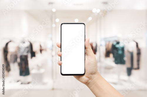 Mockup white blank screen mobile phone. Hand holding smartphone with blurred women clothing store background for your advertisement artwork.