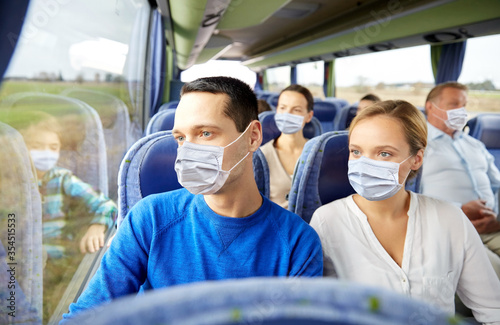 transport, tourism, road trip and people concept - couple wearing face protective medical masks for protection from virus disease with group of passengers or tourists in travel bus © Syda Productions