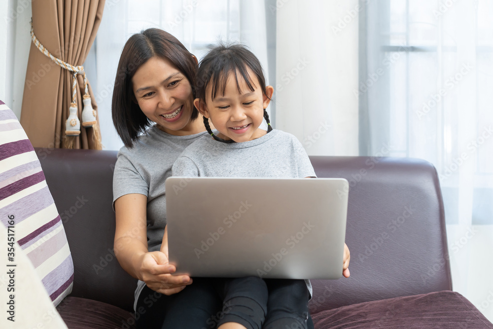 Asian mother and daughter using laptop studying homework online lesson at home, Social distance online education idea concept