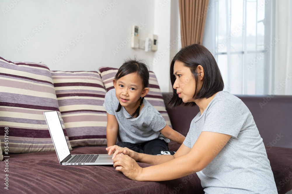 Asian mother and daughter using laptop studying homework online lesson at home, Social distance online education idea concept