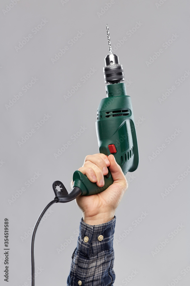 repair, construction and building tools concept - close up of builder's hand holding electric drill or perforator over grey background repair, construction and building tools concept - close up of builder's hand holding electric drill or perforator over grey background