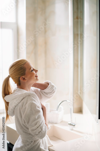 Beautiful woman enjoying in hotel. Young happy women in bathrobe use the cream for the body.	