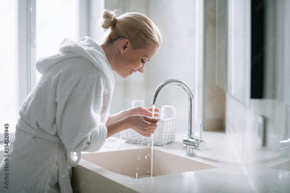 Beautiful woman enjoying in hotel. Young happy woman in bathrobe wash her hands. Beautiful woman enjoying in hotel. Young happy woman in bathrobe wash her hands.