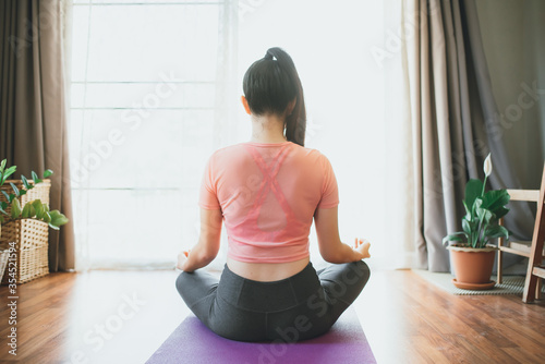 Beautiful attractive young asian woman wearing sportswear practicing yoga mats at home in the living room in the morning. Sport and recreation concept. 