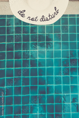 Wallpaper Mural Straw hat with Do not disturb wording at the pool edge with palm reflections in the water. Relax vacation, sun protection, travel fashion concept Torontodigital.ca