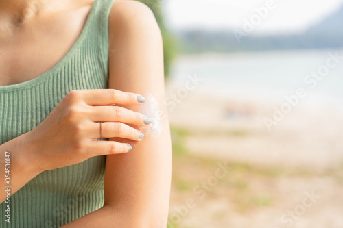 close up front view of woman applying sunscreen lotion to skin at beach in holiday for protect about sunlight , healthy lifestyle and summer season concept photo