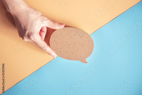 Talk bubble speech icon. Hand holding blank empty bubbles design elements on blue and yellow background. Chat on line symbol. copy space.