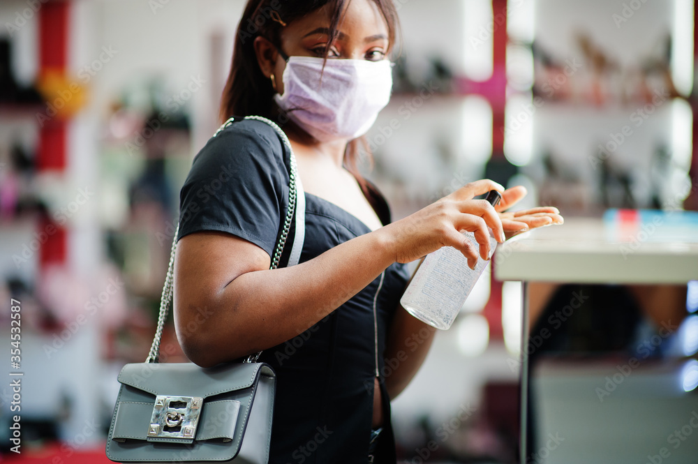 African american woman wearing face protective medical mask for protection from virus disease in shoes store use hand sanititzer during coronavirus pandemia.