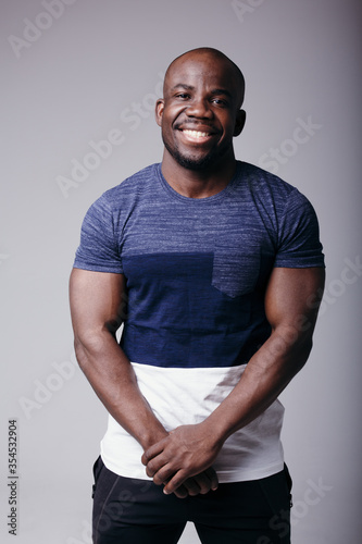 Portrait of a black man in a colored T-shirt holding his hands near his stomach and smiling at the camera in the studio