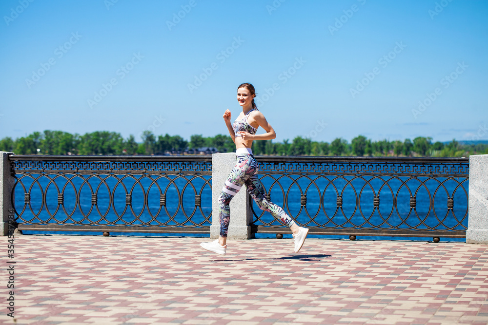 Young beautiful woman jogging along the promenade in the hot summer