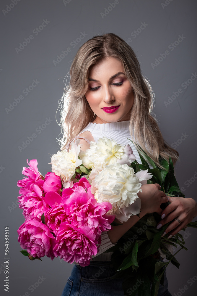 Skin care concept. Photo of blonde girl with pink peonies on grey background Skin care concept. Photo of blonde girl with pink peonies on grey background