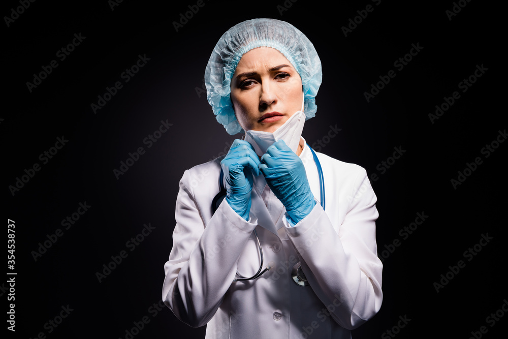 Photo of tired exhausted lady doc hold arms taking off protective mask after last late operation breathe in fresh air wear gloves lab white coat surgical cap isolated black color background Photo of tired exhausted lady doc hold arms taking off protective mask after last late operation breathe in fresh air wear gloves lab white coat surgical cap isolated black color background