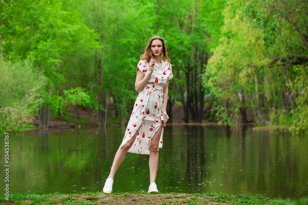 Portrait of a young beautiful woman in white dress posing by the lake