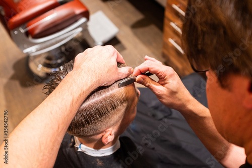 Barber shaves the parting of man's hair with razor blade