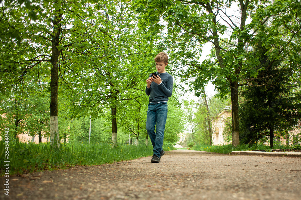A teenager is walking in the park with a phone in his hand. A teenager is walking in the park with a phone in his hand.