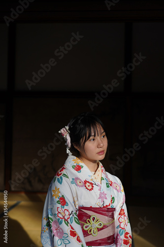 Young lady in white kimono sitting in Japanese house with dark background.