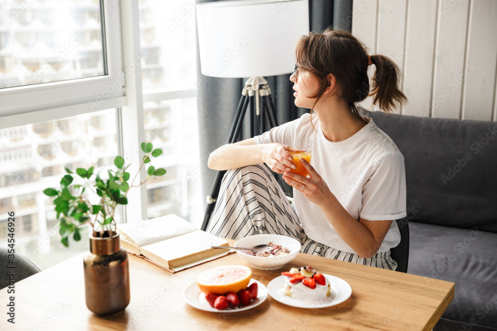 Photo of woman reading book and drinking juice while having breakfast