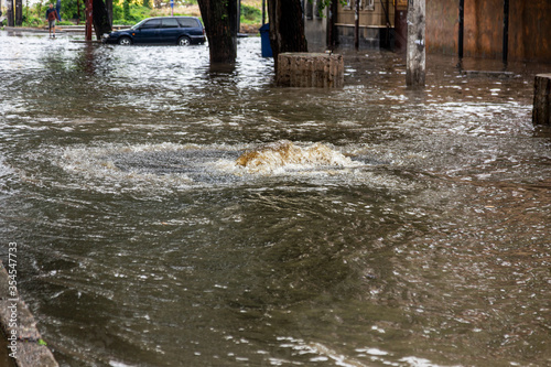 Flooding after heavy rains in city. Sewage broke open asphalt and blew up fountain. Dirty sewage broke through storm sewer and spilled onto streets of city after rain. Danger of epidemic and infection