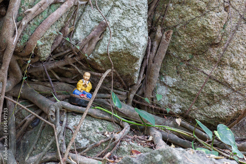 Praying Buddha mini statue between tree roots and rocks. At Nanputuo Temple, Xiamen