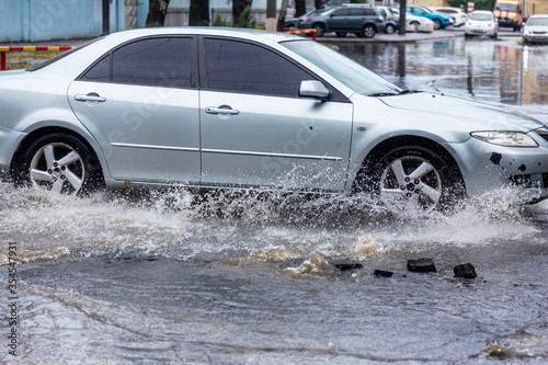   riving car on flooded road during flood caused by torrential rains. Cars float on water  flooding streets. Splash on car. Flooded city road with large puddle.  Flooding after heavy rains at city