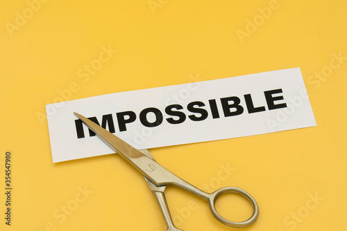 Cut impossible to possible concept. Scissors to cut paper written impossible on yellow background