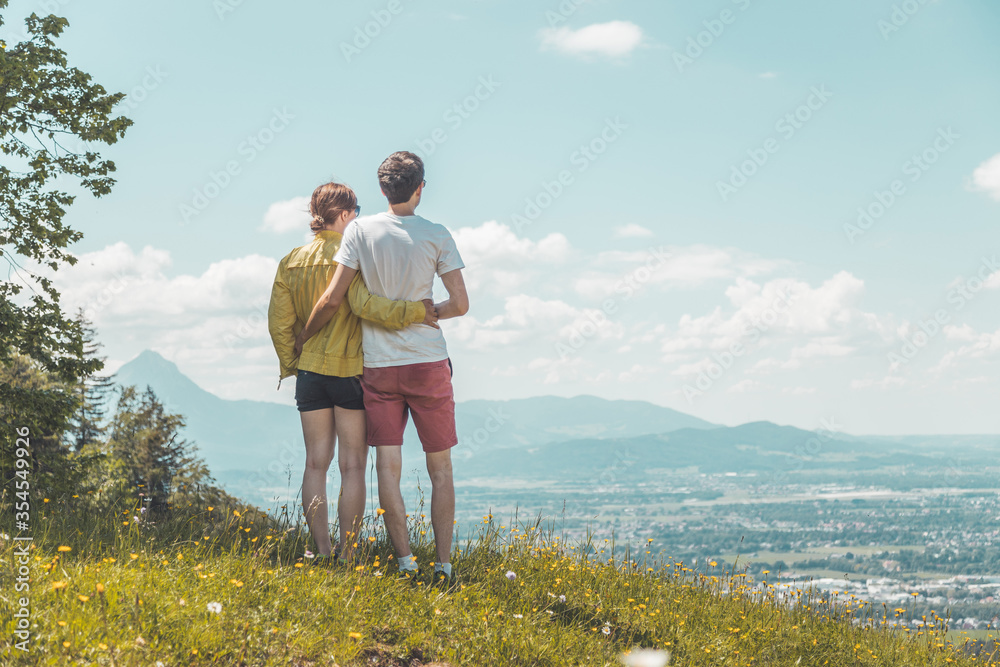 Enjoying the idyllic mountain landscape: Couple is standing on idyllic meadow and enjoying the view over the far away city of Salzburg