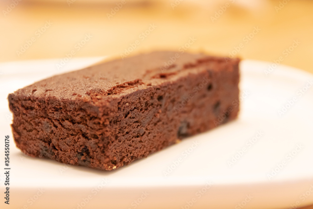 Delicious dark chocolate brownie on white plate with warm lighting at bakery shop. 