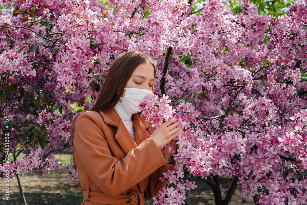 A young girl takes off her mask and breathes deeply after the end of the pandemic on a Sunny spring day, in front of blooming gardens. Protection and prevention covid 19 A young girl takes off her mask and breathes deeply after the end of the pandemic on a Sunny spring day, in front of blooming gardens. Protection and prevention covid 19
