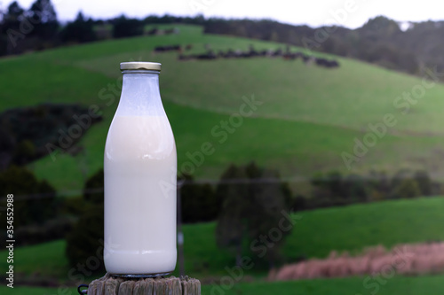 A bottle of milk with a green farm in the background. 