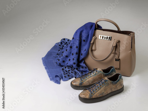 Crocodile leather sneakers next to a leather bag and a woolen scarf, side view