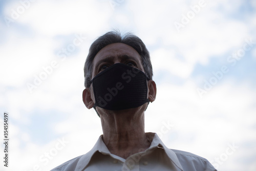 Low angle view of Indian old man with corona virus protective mask below the blue cloudy sky. Home isolation and Indian lifestyle