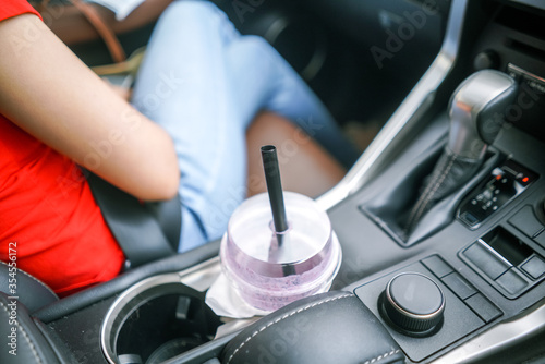 woman sitting on passenger seat inside luxury car with glass of drink in cup holder