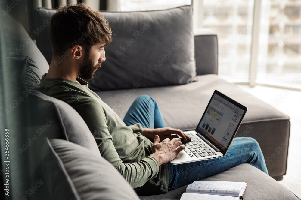 Image of man working with diary and laptop while sitting on sofa