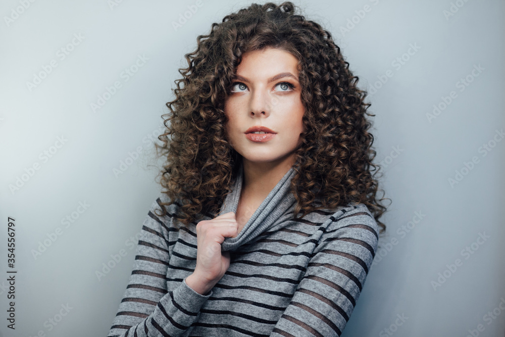Young curly girl smiling and disperses his hair in a gray sweater on a white background Young curly girl smiling and disperses his hair in a gray sweater on a white background