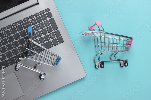 Online shopping. Laptop with supermarket trolleys on a blue pastel background. Top view. Flat lay