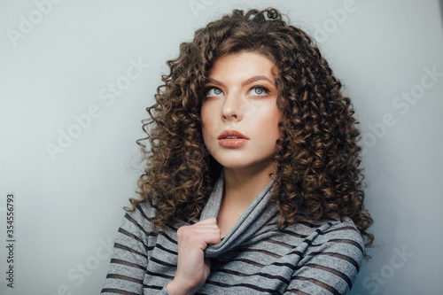 Young curly girl smiling and disperses his hair in a gray sweater on a white background