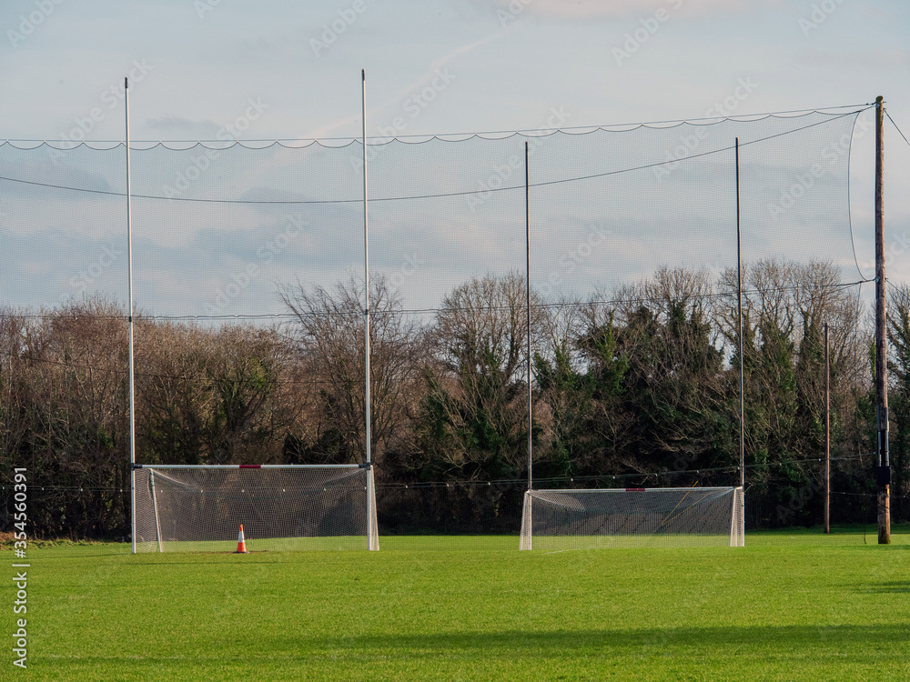 Fototapeta premium Two goal post for Irish National sports camogie, hurling, rugby and football. Green grass training pitch. Cloudy sky. Nobody.