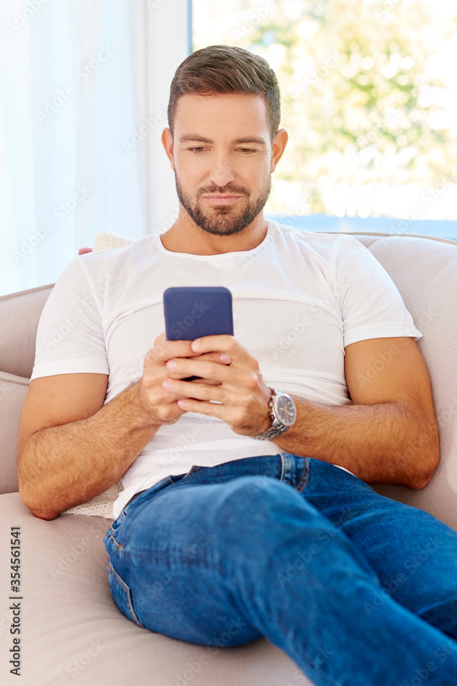 Young man text messaging while sitting on couch at home Young man text messaging while sitting on couch at home