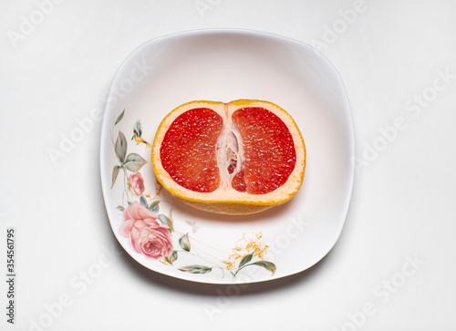 photo of the inside of one half of a pink grapefruit lying in a light plate on a light background