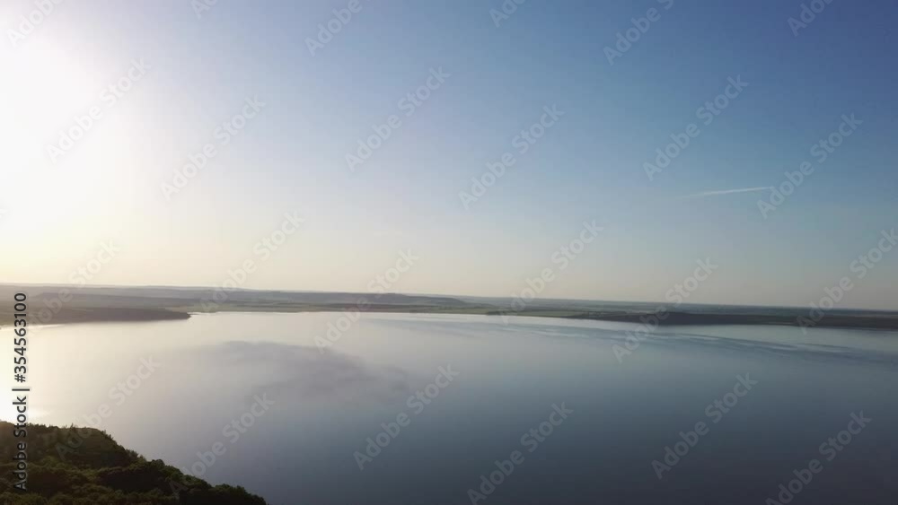 Aerial video of a lake in the mountains at sunset on a sunny summer warm day. Morning or evening in the mountains