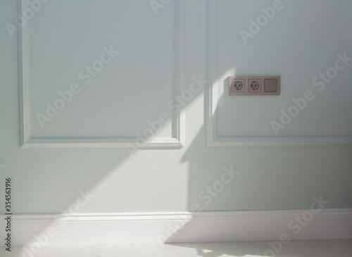 electrical outlets and a switch on the mint-colored boiserie wall lit by sunlight