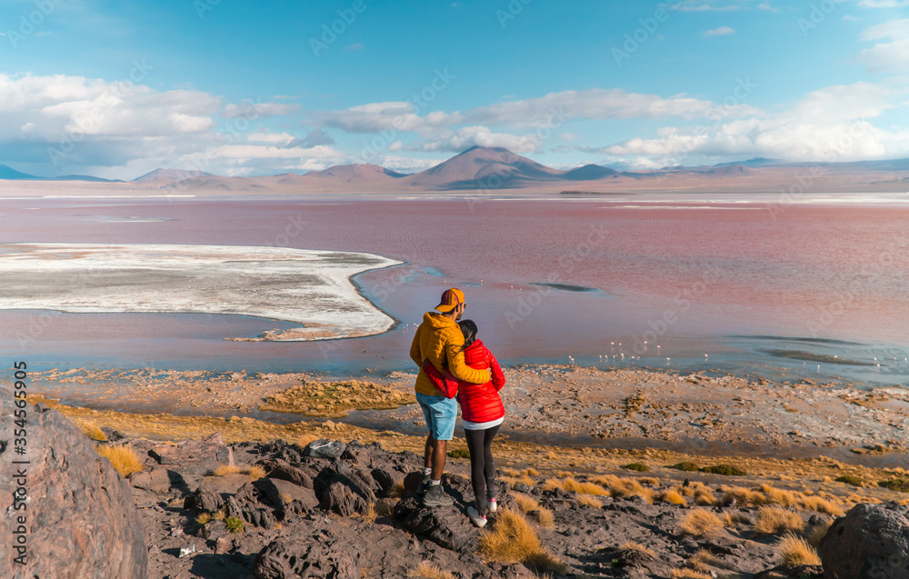Fototapeta premium Tourist couple, Red Lake mountain landscape, Bolivia. Tourists in love with Beautiful colored water, mountains background, unique scenic view. Flamingos in the lake. Uyuni, Salar de Uyuni, S America