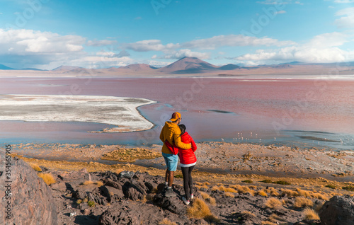 Tourist couple, Red Lake mountain landscape, Bolivia. Tourists in love with Beautiful colored water, mountains background, unique scenic view. Flamingos in the lake. Uyuni, Salar de Uyuni, S America