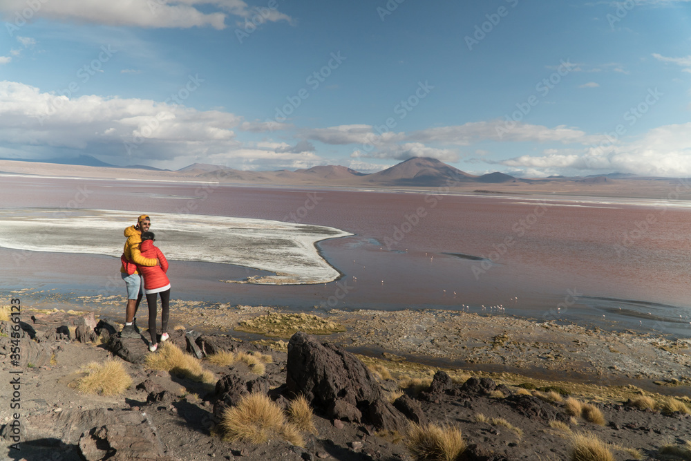 Tourist couple, Red Lake mountain landscape, Bolivia. Tourists in love with Beautiful colored water, mountains background, unique scenic view. Flamingos in the lake. Uyuni, Salar de Uyuni, S America