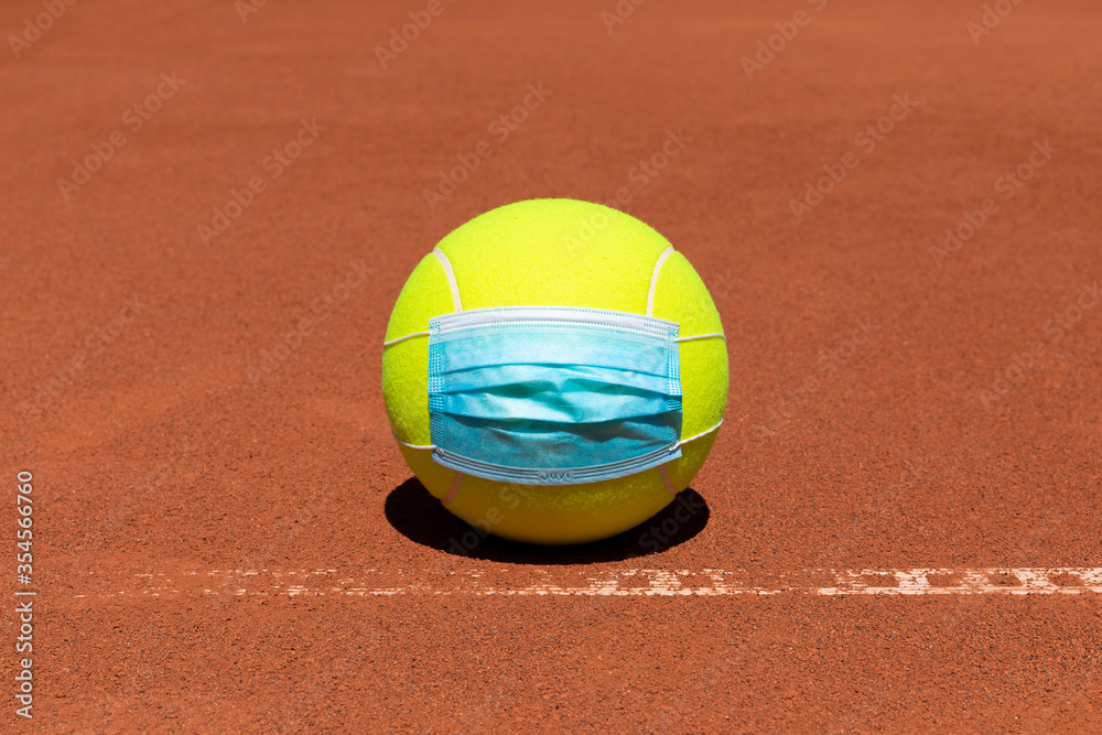 Tennis ball with mouth nose mask on a clay court